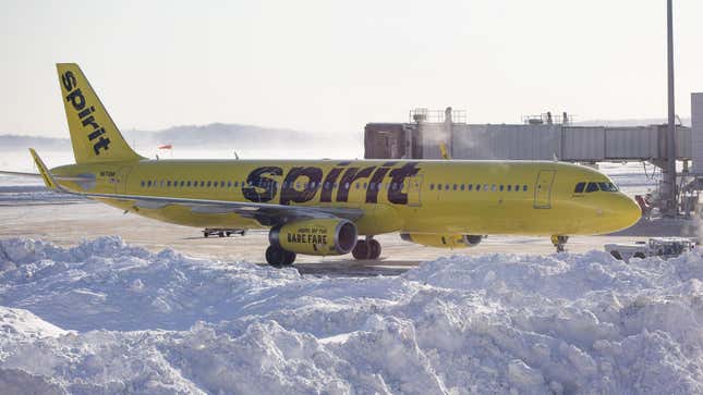 A Spirit Airlines plane sits next to a large pile of snow near an airport gate.