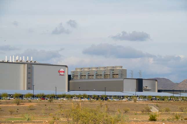 TSMC logo on a grey building beside another grey building under a grey-blue sky with clouds