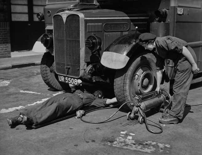 Two men under a 1941 bus in London filling the tires with air