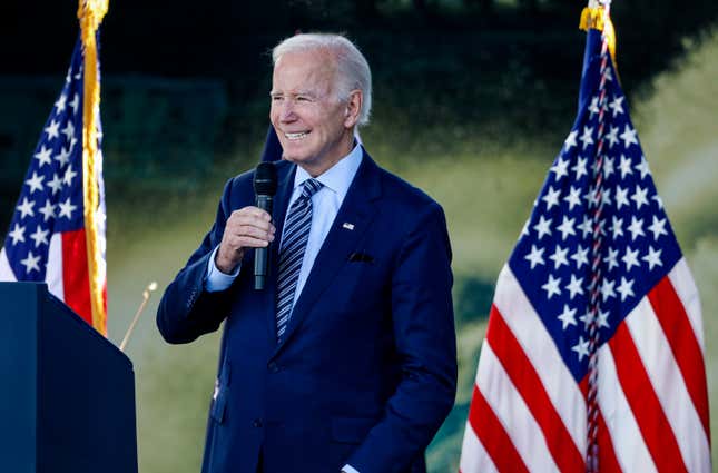 Le président Joe Biden tenant un micro debout entre deux drapeaux américains