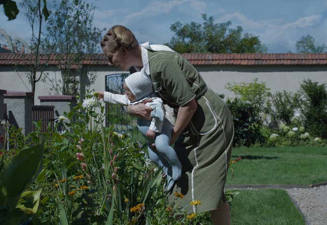 Sandra Hüller holds a baby over some flowers in a garden (The Zone Of Interest)
