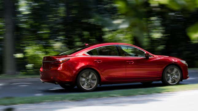 A photo of a red Mazda6 Sedan driving along a tree-lined street. 