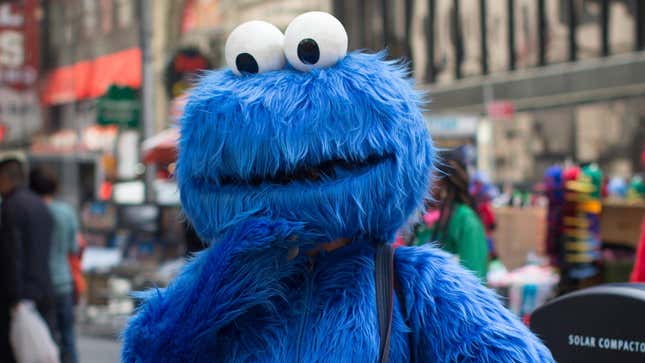 A person in a Cookie Monster costume stands with their hand to their chin.