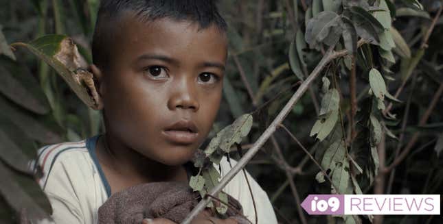A small boy stares at something startling while crouched among jungle foliage.