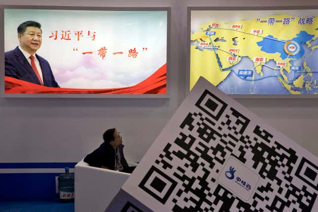 FILE - An attendee at a conference looks up near a portrait of Chinese President Xi Jinping with the words &quot;Xi Jinping and One Belt One Road&quot; and &quot;One Belt One Road strategy,&quot; in Beijing, April 28, 2017. China&#39;s Belt and Road Initiative looks to become smaller and greener after a decade of big projects that boosted trade but left big debts and raised environmental concerns. (AP Photo/Ng Han Guan, File)