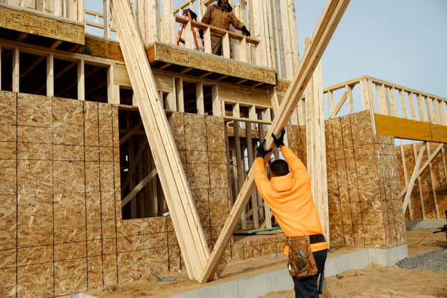 A worker moves lumber at a home under construction.