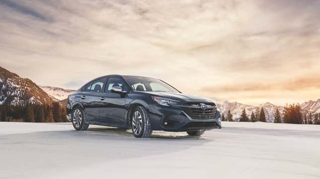 A gray Subaru Legacy parked on snow in front of snowy mountains