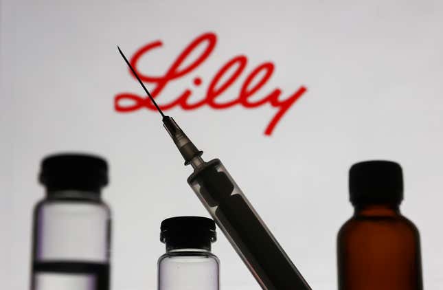 Medical bottles and syringe are seen with Eli Lilly and Company logo displayed on a screen in the background in this illustration photo.