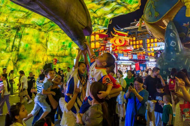 Visitors lift their children to torch a dinosaur figure on display in a new night market during a weeklong national holiday in Nanning in south China&#39;s Guangxi Zhuang Autonomous Region on Sept. 30, 2023. Tourism in China bounced back to pre-pandemic levels during a recent eight-day national holiday, giving a temporary boost to the nation&#39;s flagging economy. (Chinatopix via AP)