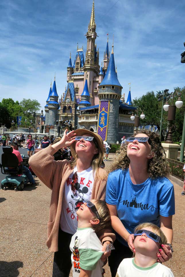 A family visiting from Sarasota watches the solar eclipse at the Magic Kingdom at Walt Disney World, in Lake Buena Vista, Fla., Monday, April 8, 2024. (Joe Burbank/Orlando Sentinel via AP)