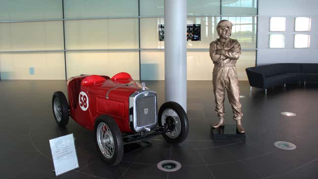 A photo of a state of McLaren founder Bruce McLaren alongside the first race car he drove. 