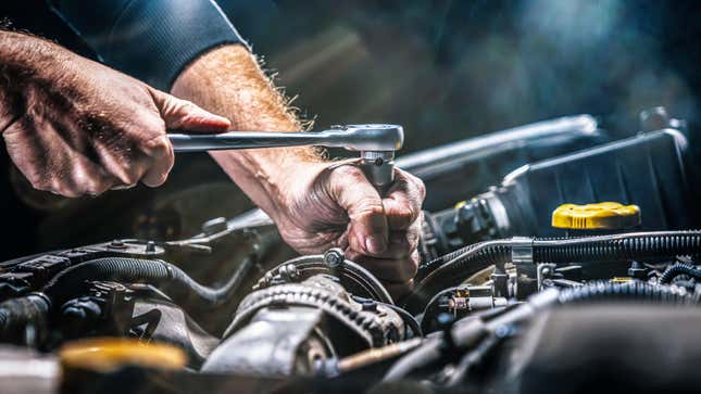 An auto mechanic working on car engine inside a mechanic's garage.