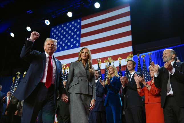 Donald Trump walks with his fist in the air and his other hand holding Melania Trump's hand as they walk in front of people clapping