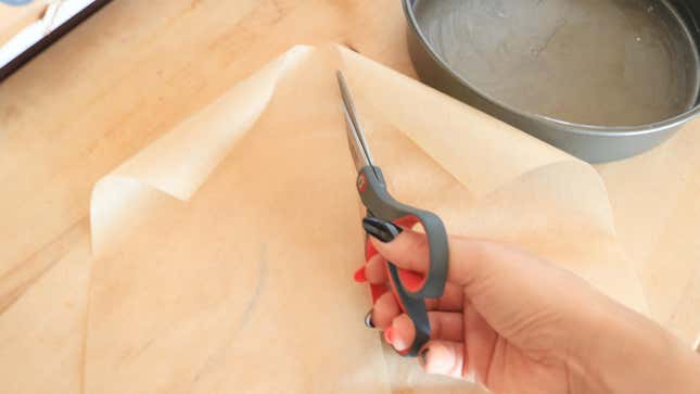 A hand cutting parchment paper with scissors.