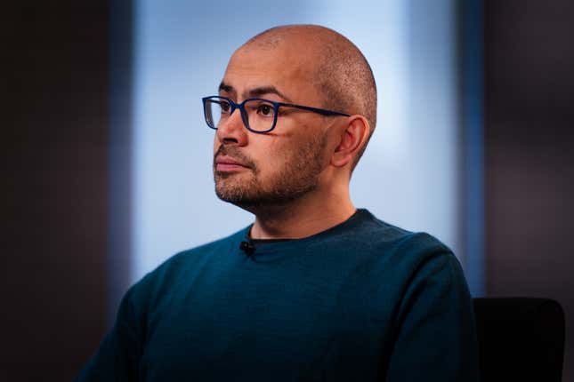 left-side profile of Demis Hassabis wearing black framed glasses and a navy shirt 