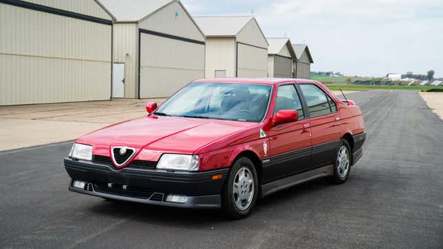 Une Alfa 164 rouge garée devant des hangars