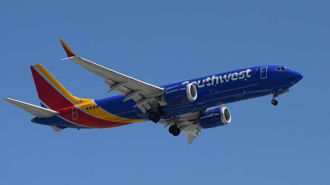 A predominantly blue Southwest Airlines plane flies in a clear blue sky