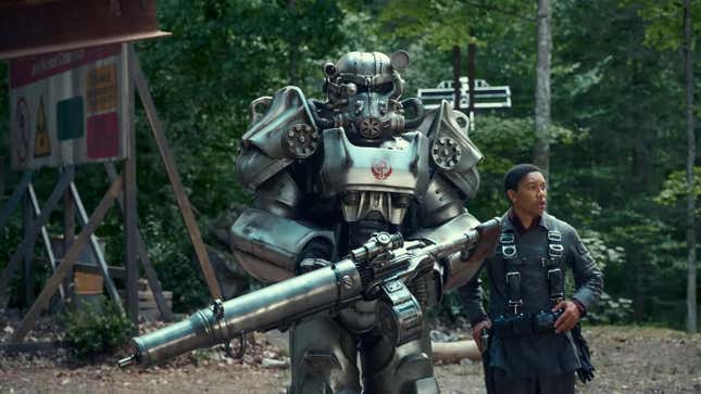 Aaron Moten as Maximus, a squire for the Brotherhood of Steel, standing next to one of Fallout's iconic power armors.