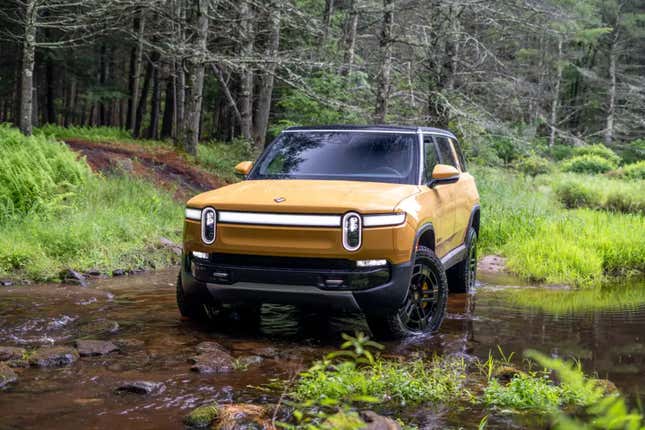 Yellow Rivian RS1 SUV fording a creak with a thick pine forest in the background.