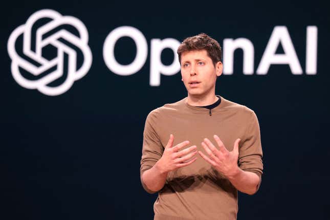 Sam Altman speaking with his hands up in front of a black backdrop that says OpenAI in white letters