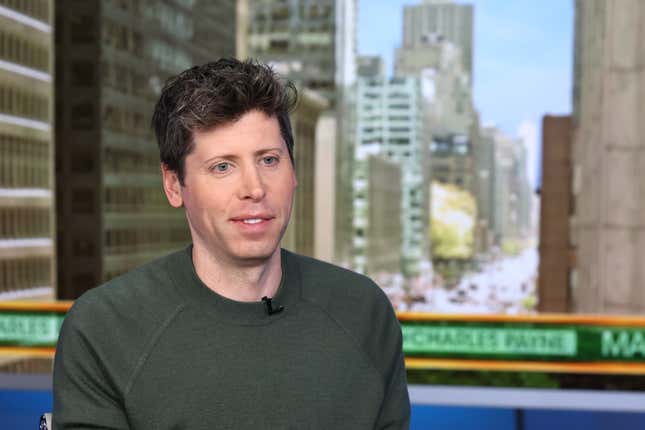 Sam Altman wearing a greenish grey sweatshirt smiling and looking out onto something