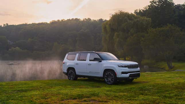 A white Jeep Grand Wagoneer in a field with trees in the background