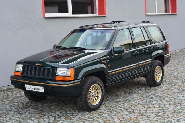 A green 1993 Jeep Grand Cherokee with gold stripe is parked on cobbles.