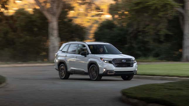 A white 2025 Subaru Forester driving in front of grass and trees