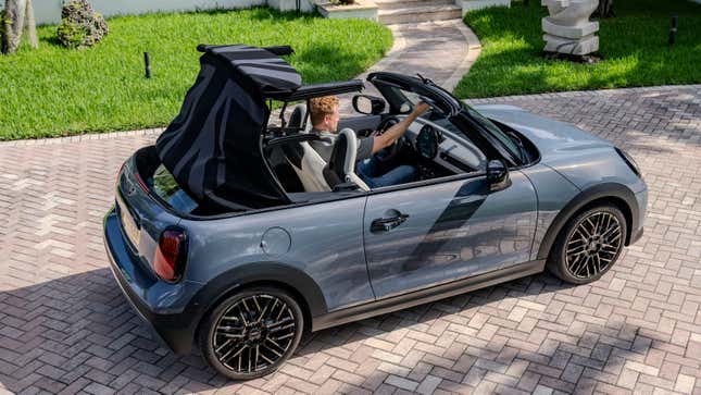 An overhead shot of a gray Mini COoper convertible with its top being retracted parked on brick