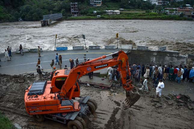 People gather next to a section of a road damaged by flood waters following heavy monsoon rains in Madian area in Pakistan’s northern Swat Valley on August 27, 2022.