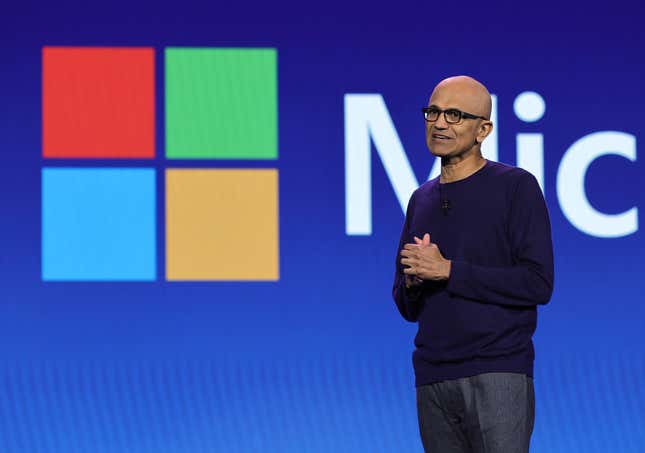 Satya Nadella in front of a backdrop with the Microsoft logo