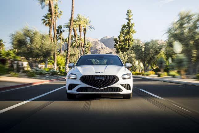 2022 Genesis G70 sedan in white driving down a desert street with mountains in the background and blurry trees