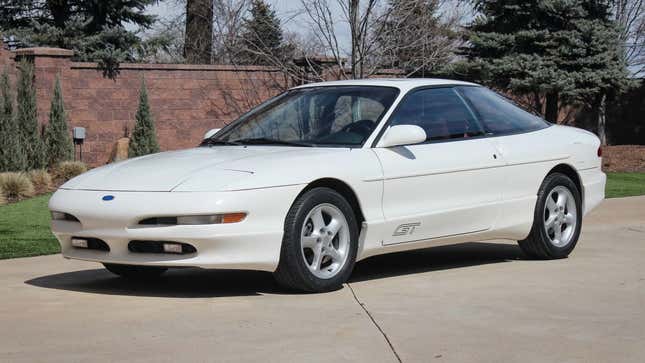 Une Ford Probe blanche garée devant une clôture