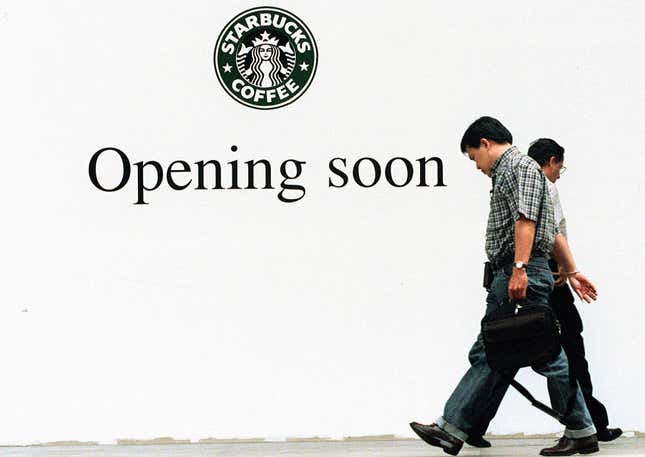 Dos hombres se cruzan frente a un anuncio que anuncia la apertura de la segunda sucursal de la cadena de cafeterías estadounidense Starbucks el 19 de mayo de 1999 en una calle de Bangkok.