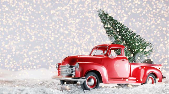 A little red toy truck hauling a Christmas tree through a snowy scene