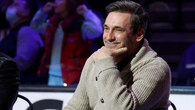 Jon. Hamm wears a tan cardigan sweater and smiles at an NHL All-Star Weekend event.