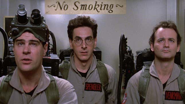 Stantz, Spengler, and Venkman stand in an elevator, waiting to bust ghosts while a sign above them reads "No Smoking.".