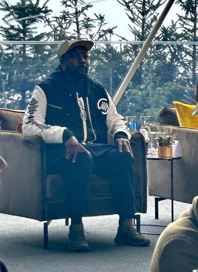 Will.i.am sits on a chair on stage at a lunch event in Davos, Switzerland with a view of the mountains behind him