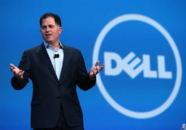 Michael Dell speaking with his hands up, a Dell logo is on the blue backdrop behind him