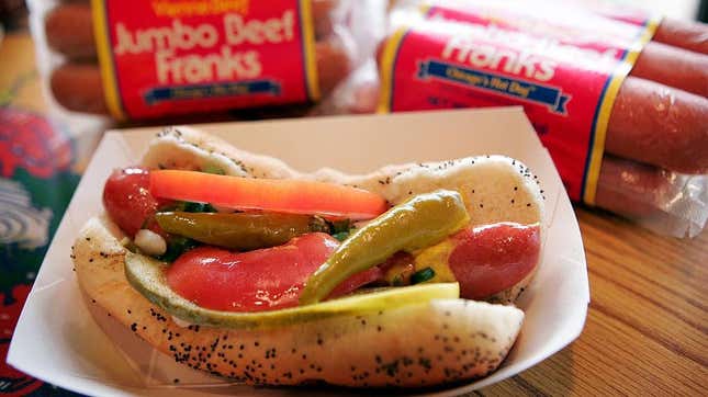 Hot dog with everything in a paper boat beside packs of Vienna Beef hot dogs