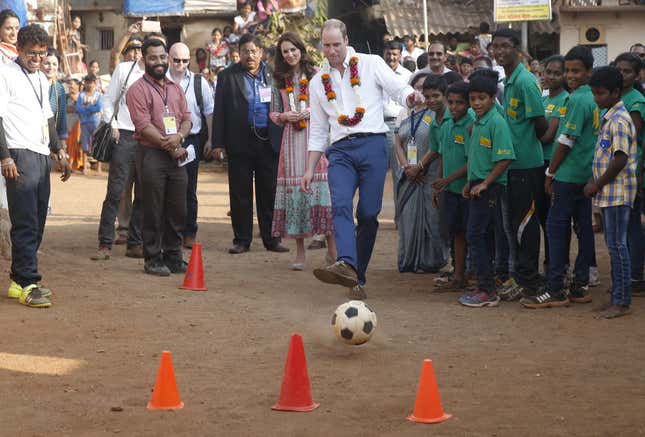 Prince William plays with a football as Kate watches during their visit to a slum in Mumbai on Apr. 10, 2016.