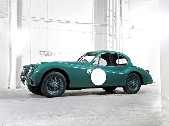 A green Jaguar XK140 coupe in front of a white concrete building interior