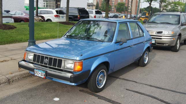 A blue 1990 Plymouth Horizon parked in front of a Oldsmobile Bravada