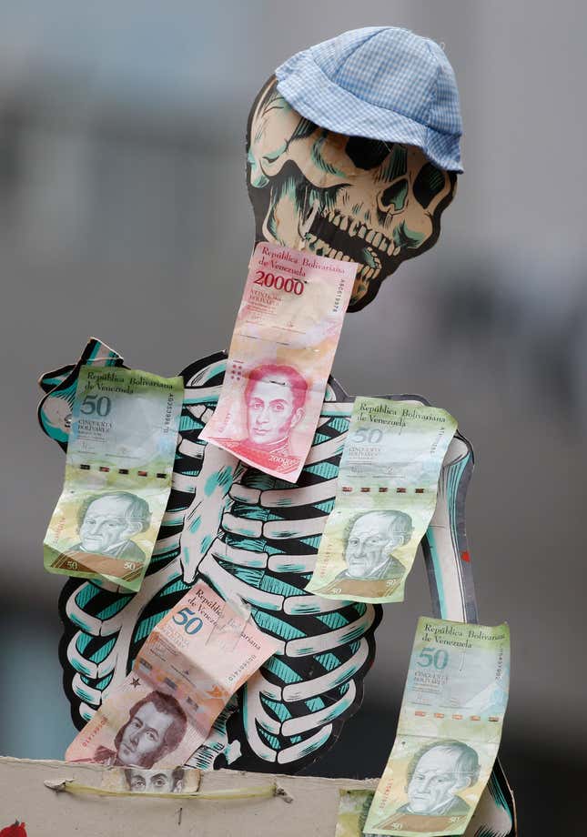 FILE - A skeleton is adorned with Venezuelan Bolivar bills to draw attention to the devaluation of the currency and hunger, during an opposition march in Caracas, Venezuela, March 10, 2020. (AP Photo/Ariana Cubillos, File)