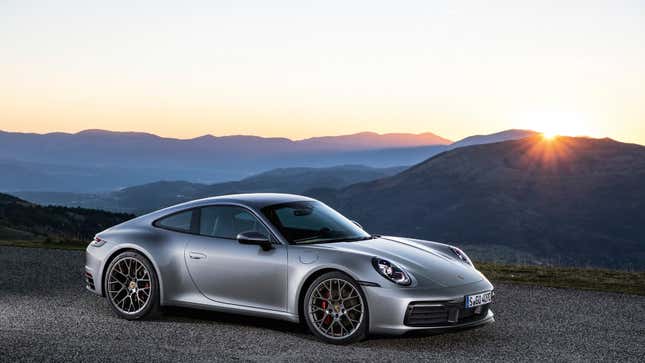 a silver Porsche 911 parked on gravel in front of a sunset in the mountains