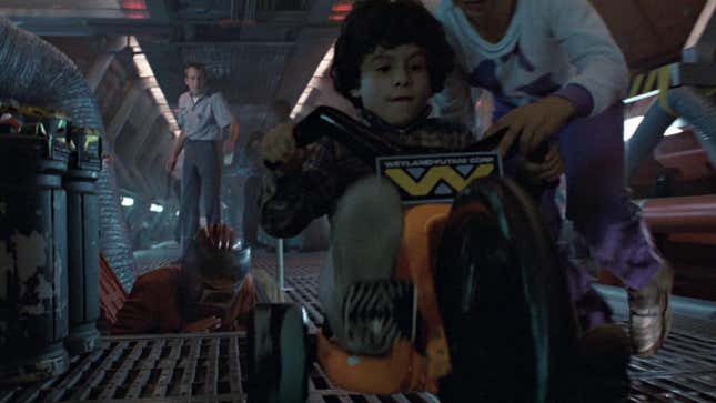 A curly-haired kid bikes down a futuristic hall while his family watches.