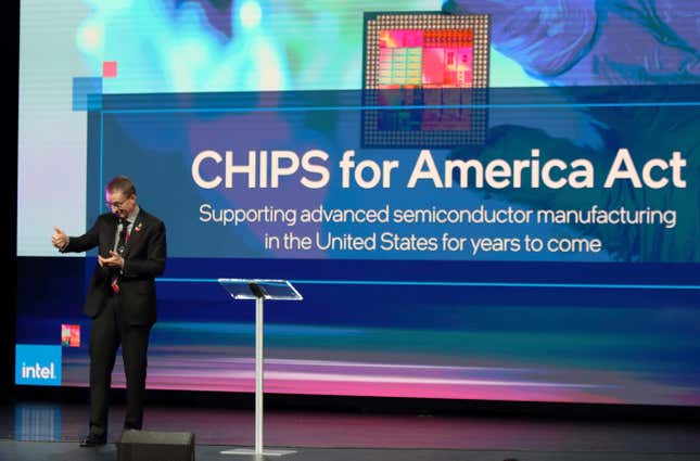 Pat Gelsinger lève le pouce devant un arrière-plan sur lequel est écrit « CHIPS for America Act : Supporting advanced semiconductor manufacturing in the United States for years to come », un petit logo Intel se trouve dans le coin inférieur gauche de l’arrière-plan et un podium se trouve au milieu de la scène