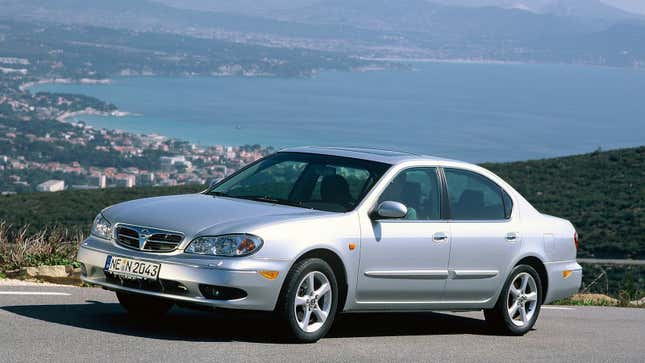  A photo of a silver Nissan Maxima sedan parked with the ocean behind it. 