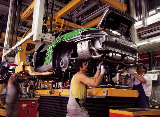 Several men in a factory assembly line are building a 996 generation Porsche