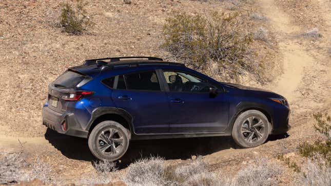 A blue crosstrek with a wheel propped up off road